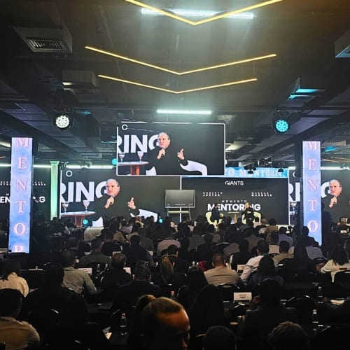evento mentoria Roberto Justus, pessoas acomodadas em cadeiras, palco ao fundo com palestrante e painéis de led